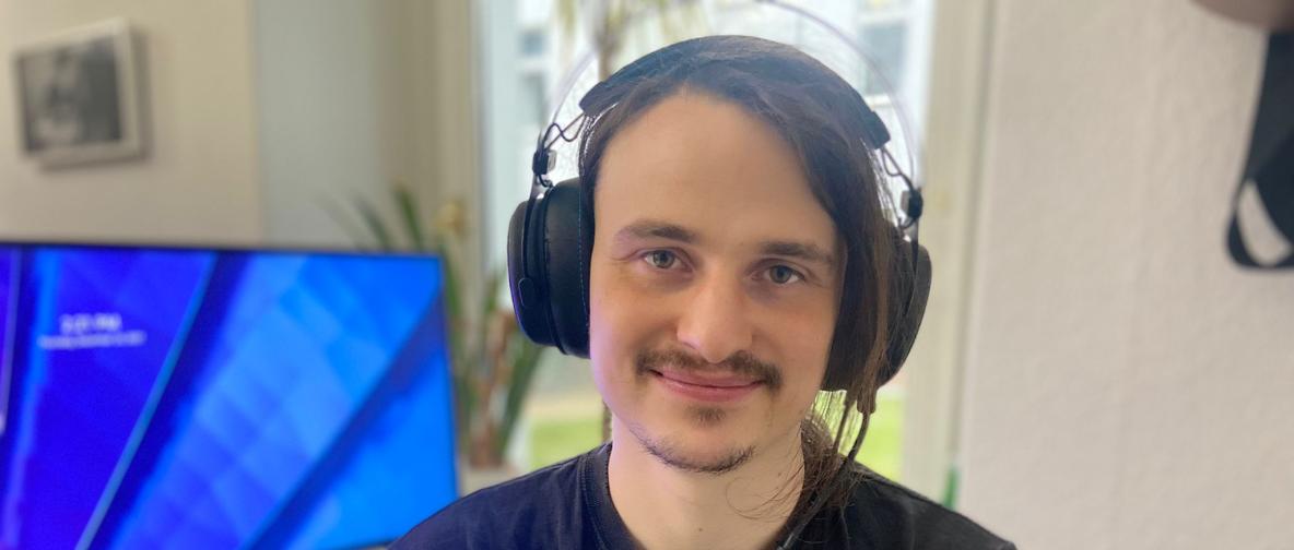 Ein Mann mit Headset sitzt neben einem Bildschirm.