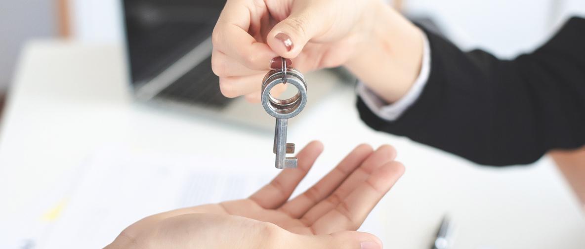 Eine Hand überreicht einer anderen Person einen großen, silbernen Schlüssel. Eine Schlüsselübergabe als Symbol für den erfolgreichen Übergang zu einer neuen Agentur bei digitalen Projekten.