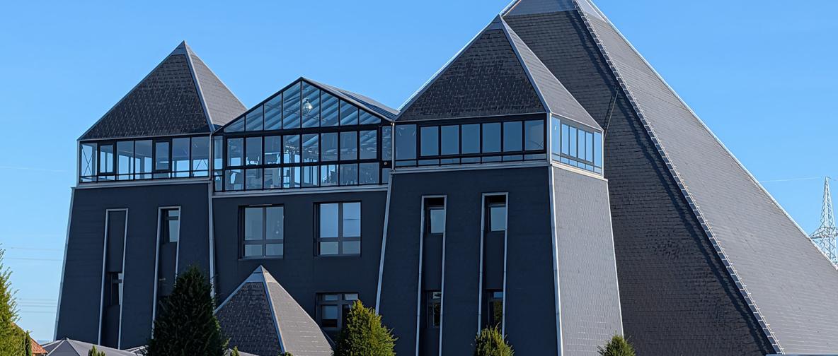 Modernes Gebäude mit pyramidenförmigen Dächern und Glasfront.