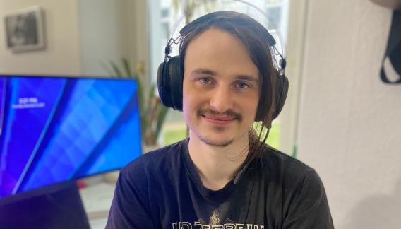 Ein Mann mit Headset sitzt neben einem Bildschirm.