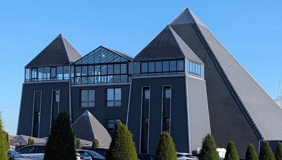 Modernes Gebäude mit pyramidenförmigen Dächern und Glasfront.