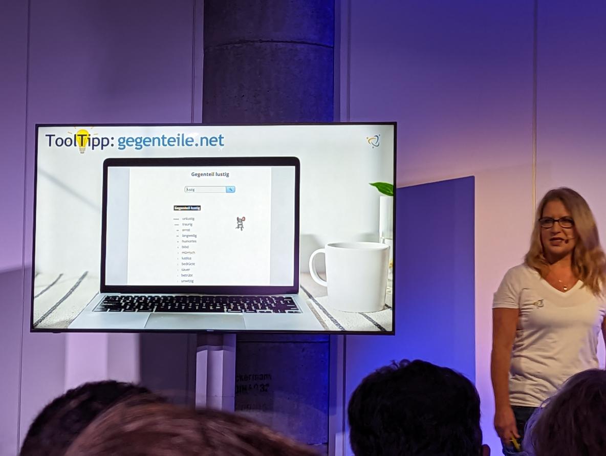 Frau auf der Bühne vor einem Monitor mit einer Slide zum Onlinetool gegenteile.net