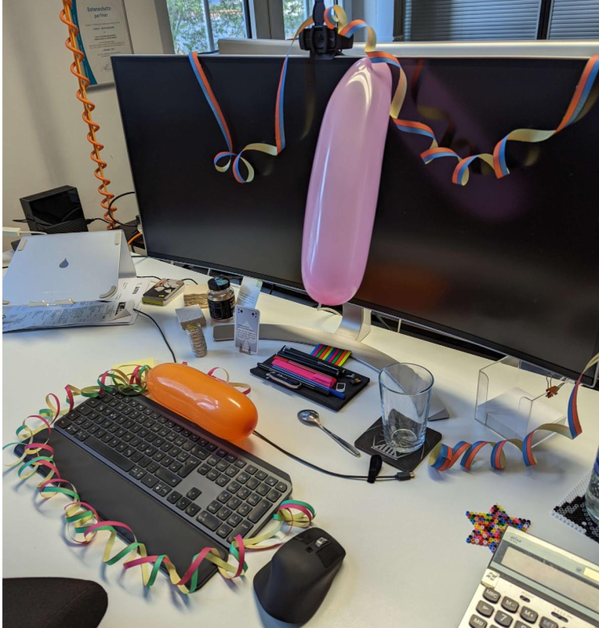 Geschmückter Arbeitsplatz. Luftschlangen und Ballons hängen am Monitor.