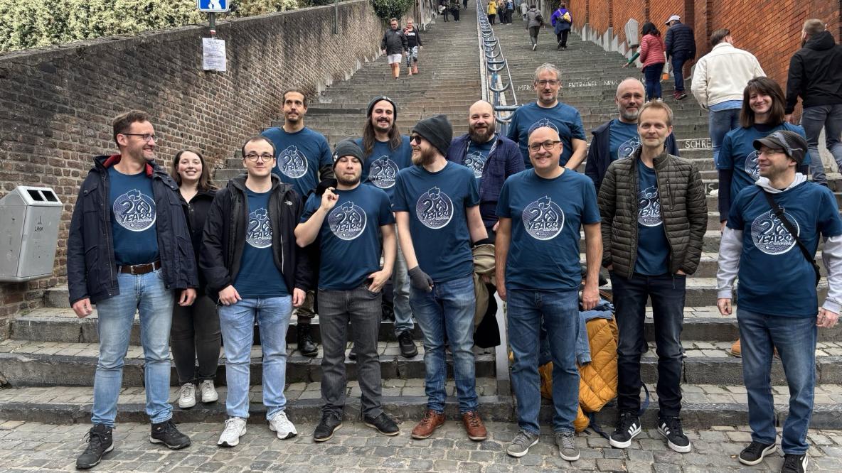 Das erdfisch-Team steht gemeinsam auf der Montagne de Bueren in Lüttich. Alle tragen dunkelblaue T-Shirts mit dem Aufdruck ‚20 Years of erdfisch‘. Im Hintergrund die lange Treppe, einige Passant:innen.