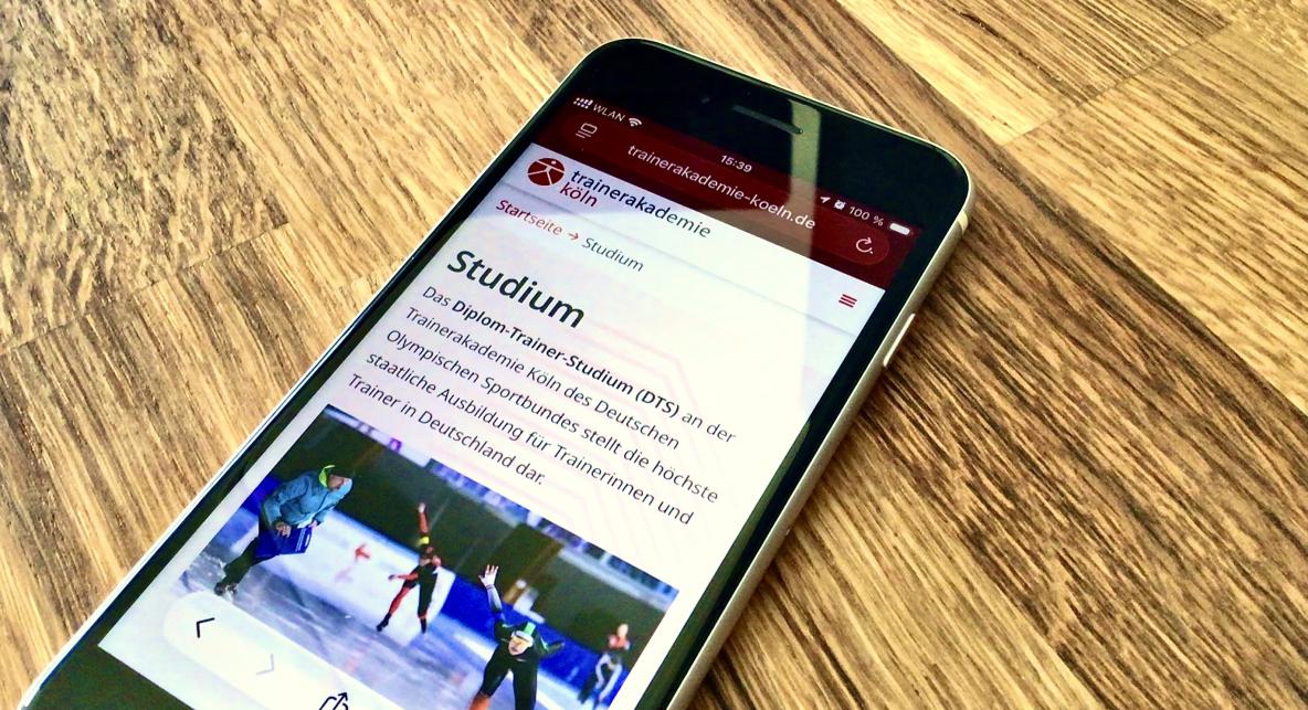 Smartphone mit Webseite der Trainerakademie Köln auf einem Holztisch